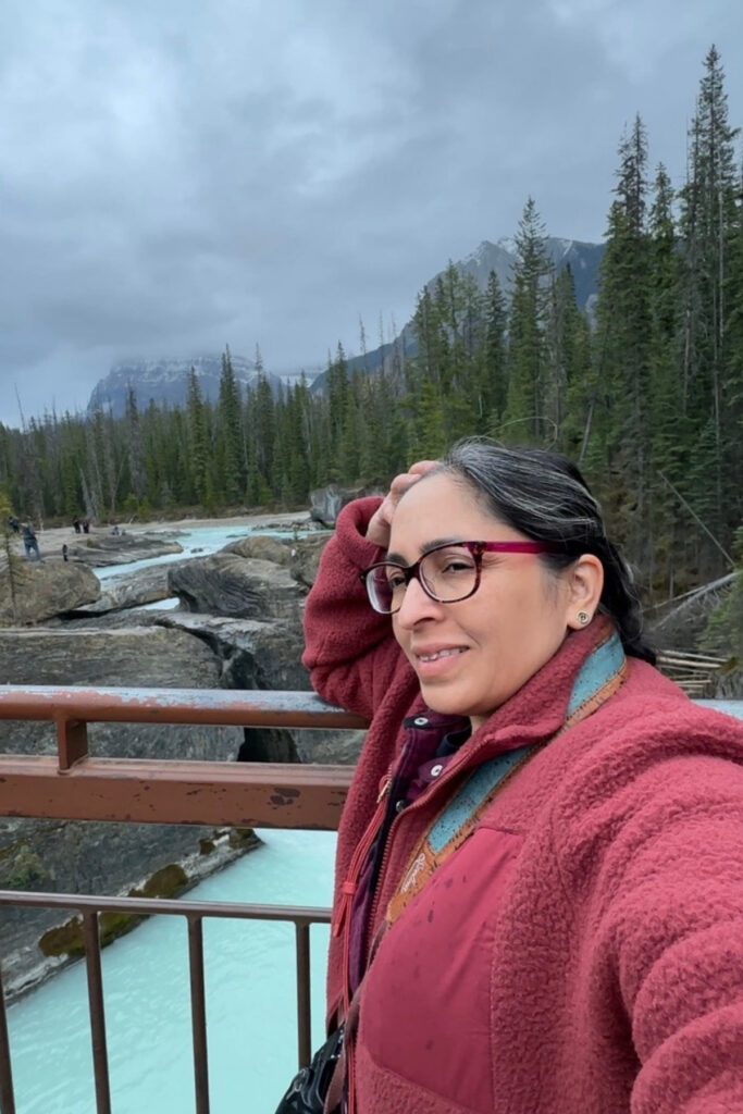 Travel writer beside the Natural Bridge viewpoint in Yoho National Park, with turquoise Kicking Horse River water flowing through carved rock formations.